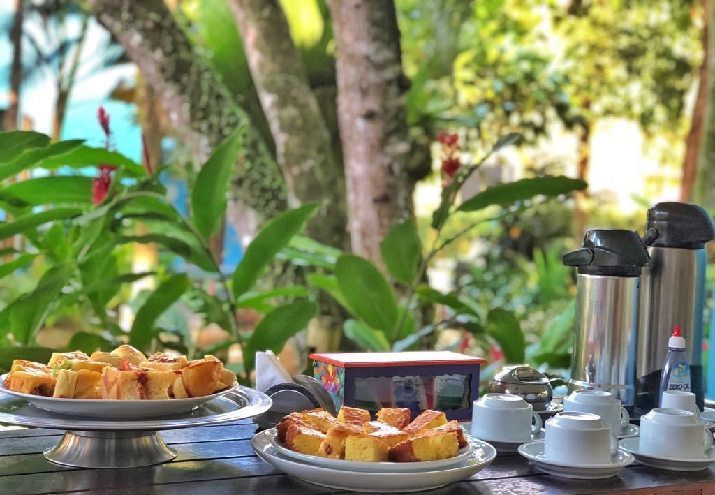 A breakfast setup with toast, a coffee maker, and a teapot on a table with a view of trees and greenery.