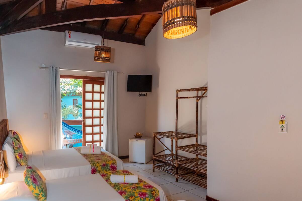 A hotel room with two beds, a TV, a wooden shelf, and a view of a blue building outside.