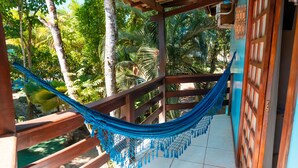 A hammock tied between wooden beams, overlooking a lush garden with various tropical plants.