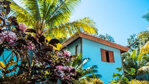 A small, single-story building with a blue exterior and a red roof, surrounded by lush tropical vegetation.