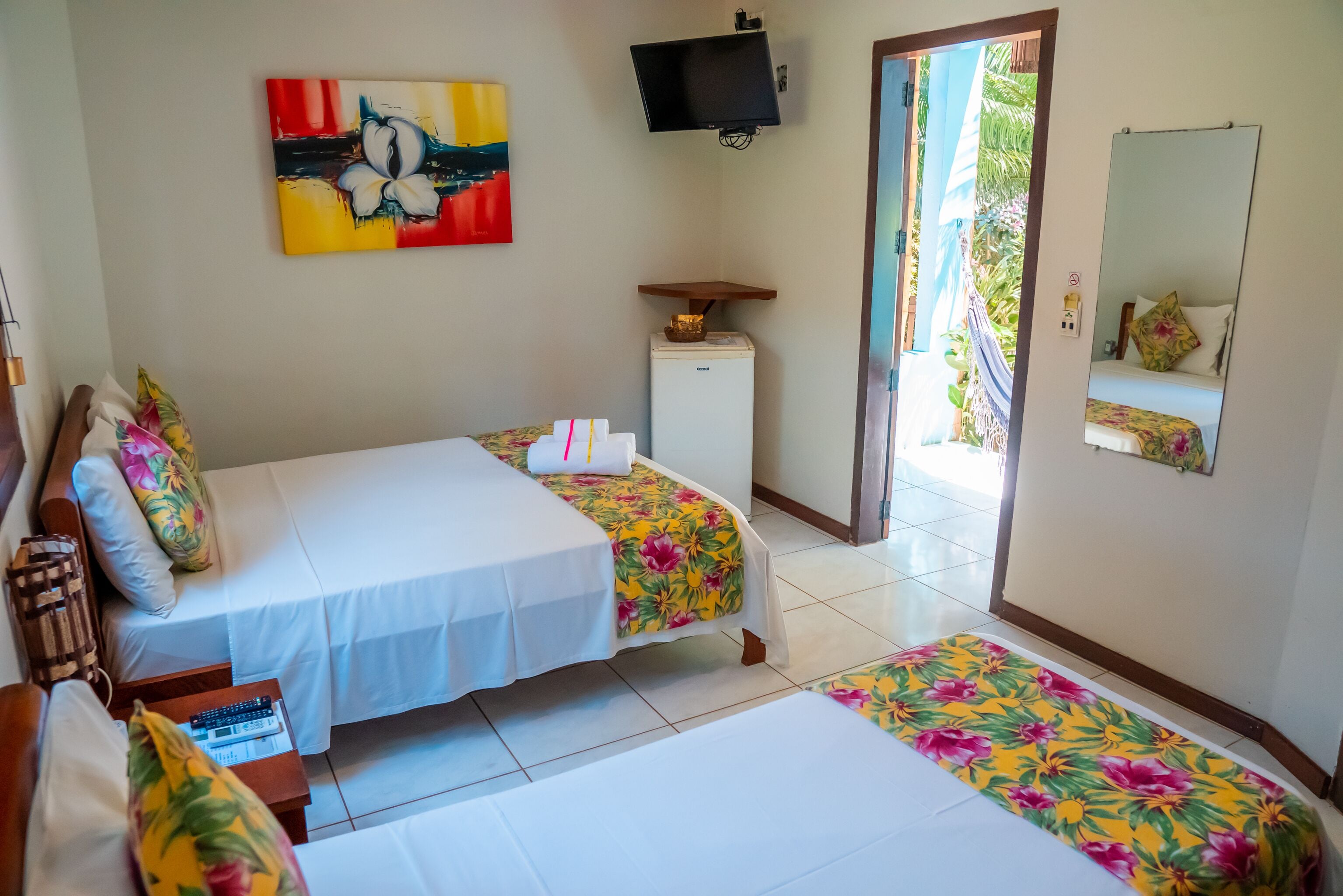 A hotel room with two beds, a small refrigerator, a flat-screen TV, and a large window with a view of palm trees.
