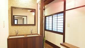 A bathroom with a wooden vanity, a mirror, and a window with blinds. - Tenma Itoya Guest House - Hostel (Osaka)