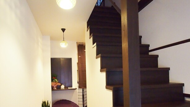 A wooden staircase with a dark finish, white walls, and a hanging light fixture. - Tenma Itoya Guest House - Hostel (Osaka)