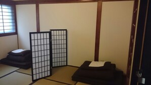A traditional Japanese room with tatami flooring, a shoji screen, a tatami mat sofa, and a small tatami mat stool. - Tenma Itoya Guest House - Hostel (Osaka)