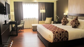 Una habitación de hotel con cama, escritorio, silla, televisor y ventana con cortinas.