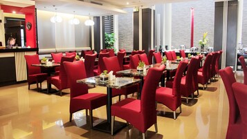 Un restaurante moderno con sillas y mesas rojas, una barra con un reloj y una planta en la esquina.