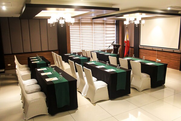A conference room with long tables, chairs, and a projector screen. - Brentwood Suites (Quezon City)