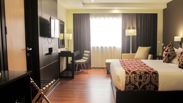 Una habitación de hotel con cama, escritorio con silla, televisión y armario.
