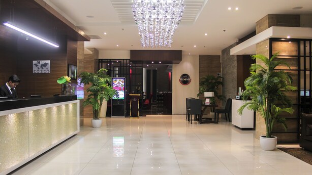 Een modern ingerichte hotelontvangsthal met een receptiebalie, een kroonluchter en potplanten.