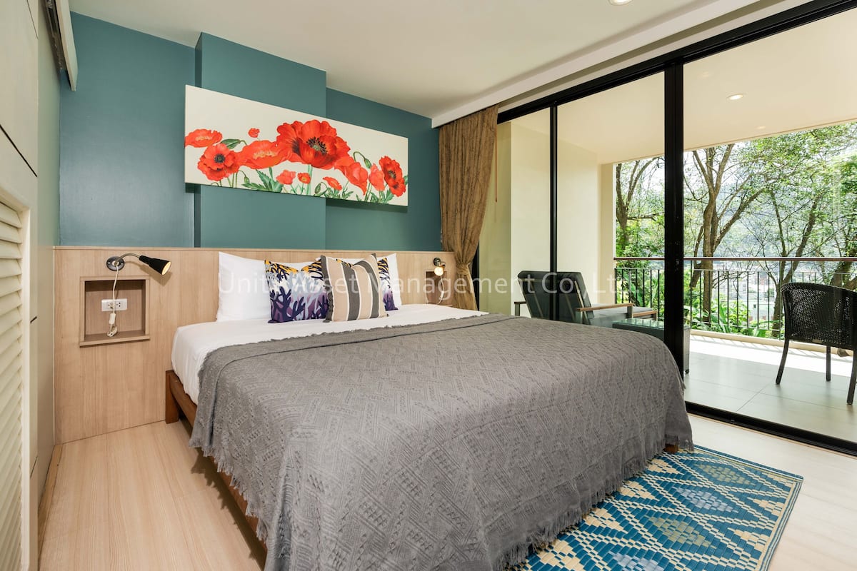 A modern bedroom with a large bed, a painting of red flowers, and a view of greenery through the balcony.