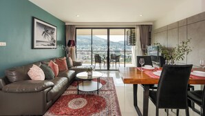 A modern living room with a sofa, coffee table, and dining area. - The Unity & The Bliss Patong Residence (Patong)