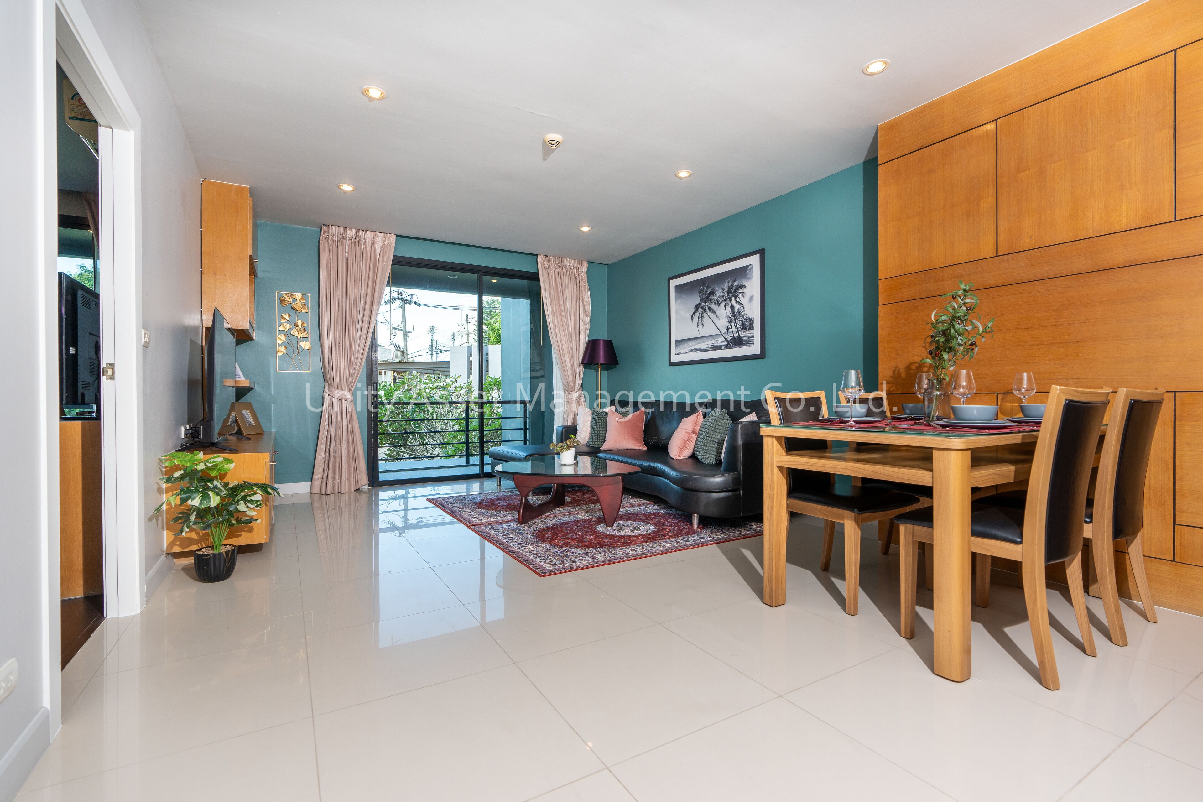A modern living room with a dining area, teal walls, wooden paneling, a large window, and a view of greenery.