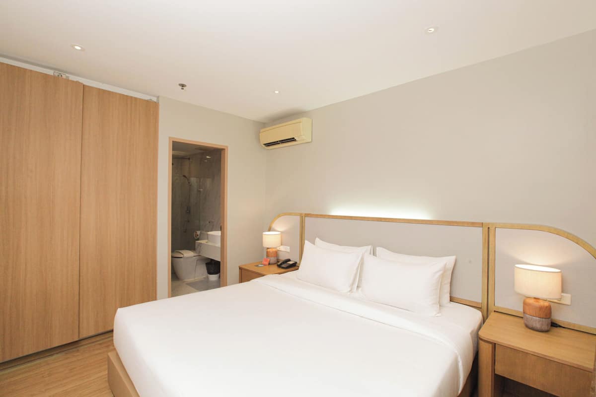 Une chambre d’hôtel avec un grand lit, une armoire en bois et deux tables de chevet avec des lampes.