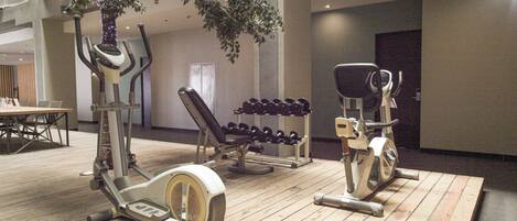 Un gimnasio con máquinas de cardio, mancuernas y una banca.
