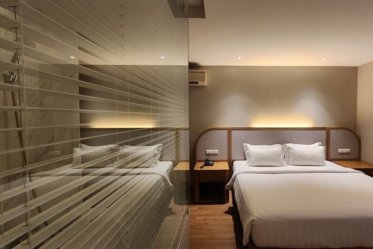Une chambre d’hôtel équipée d’un lit, de tables de chevet, d’un climatiseur fixé au mur et d’une fenêtre avec des stores.