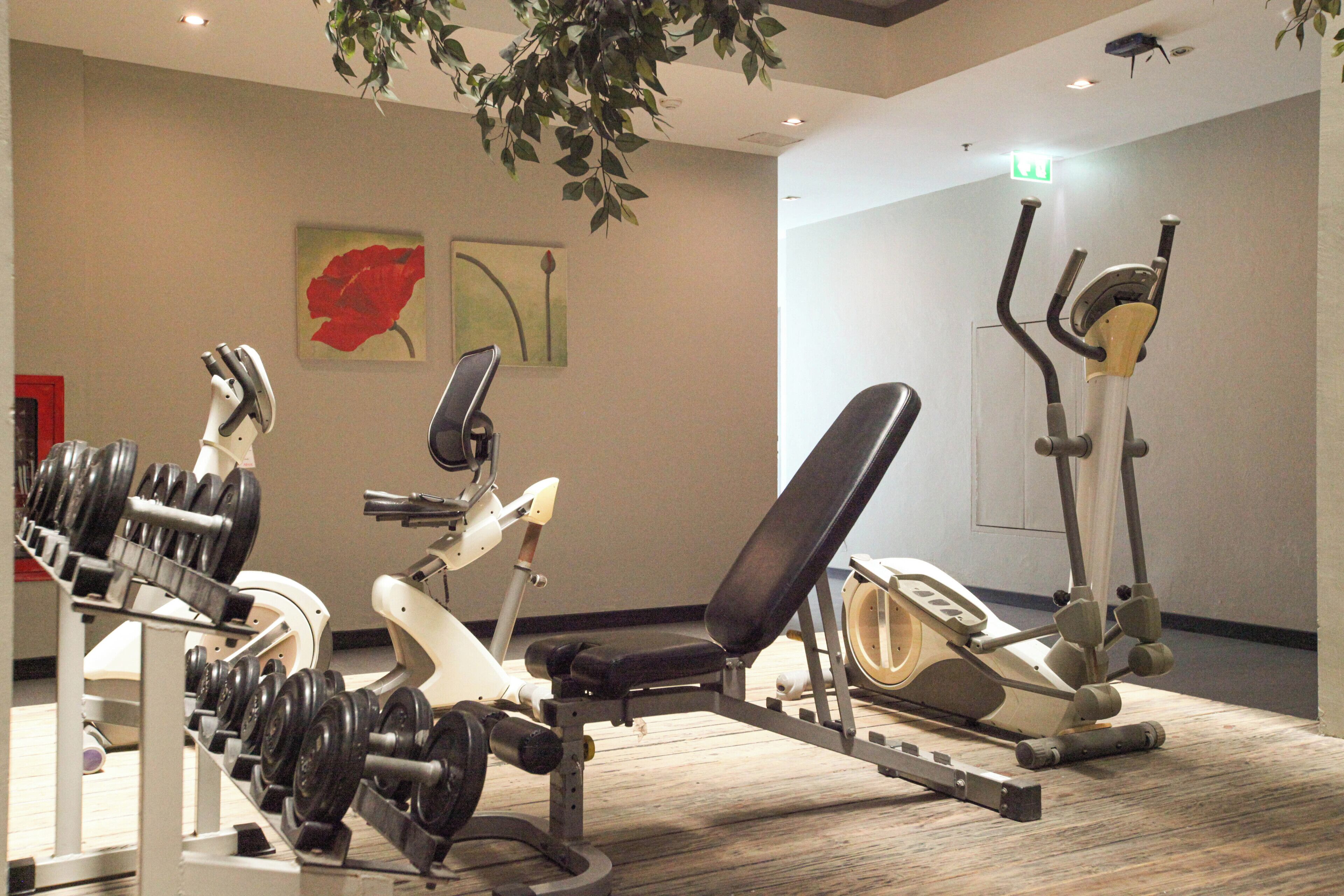 Ein Fitnessraum mit unterschiedlichen Trainingsgeräten, darunter Hanteln, eine Bank und Cardiogeräte.