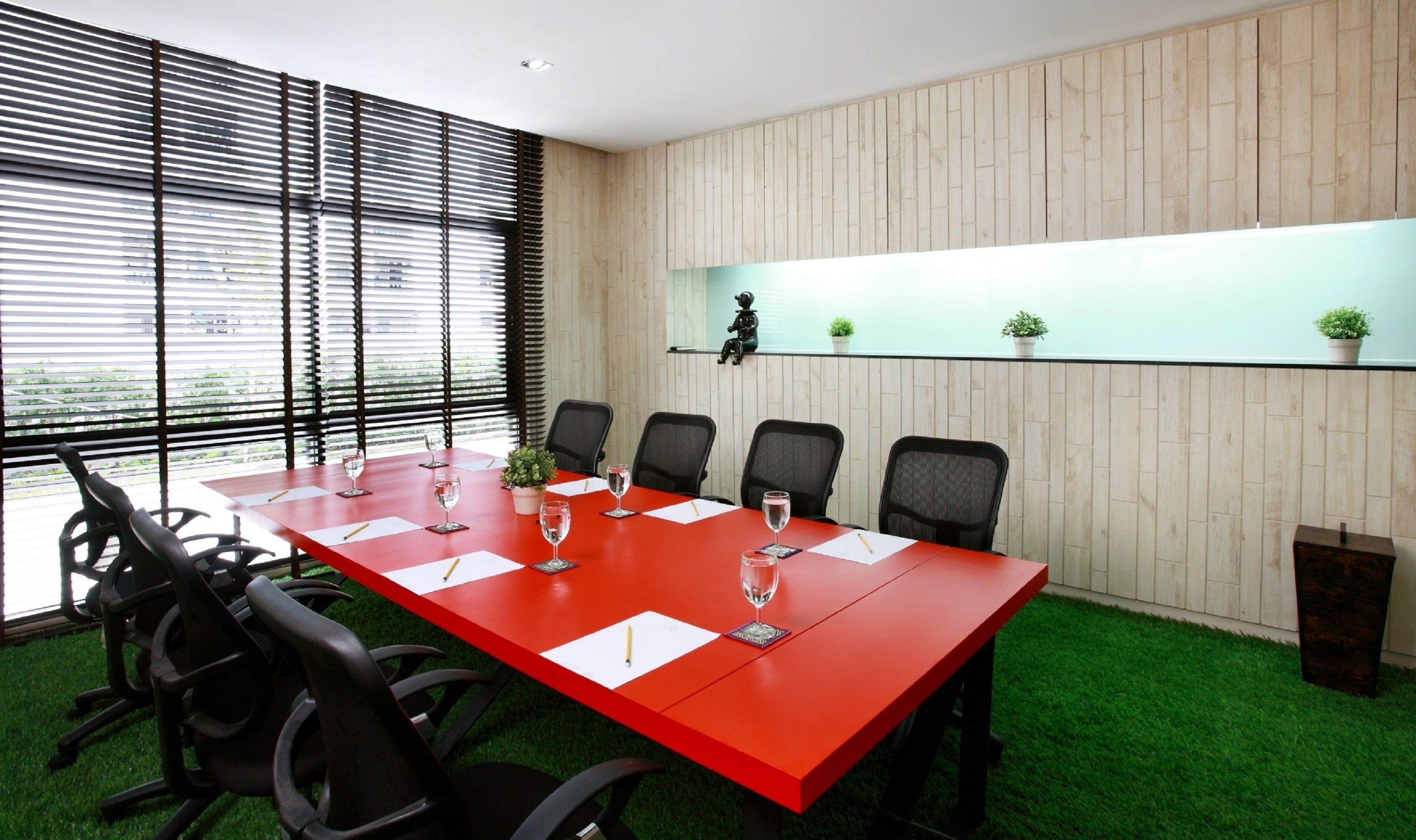 A conference room with a red table, black chairs, and a wooden wall with a shelf.