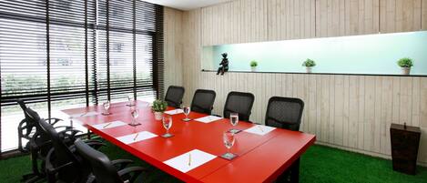 A conference room with a red table, black chairs, and a wooden wall with a shelf.
