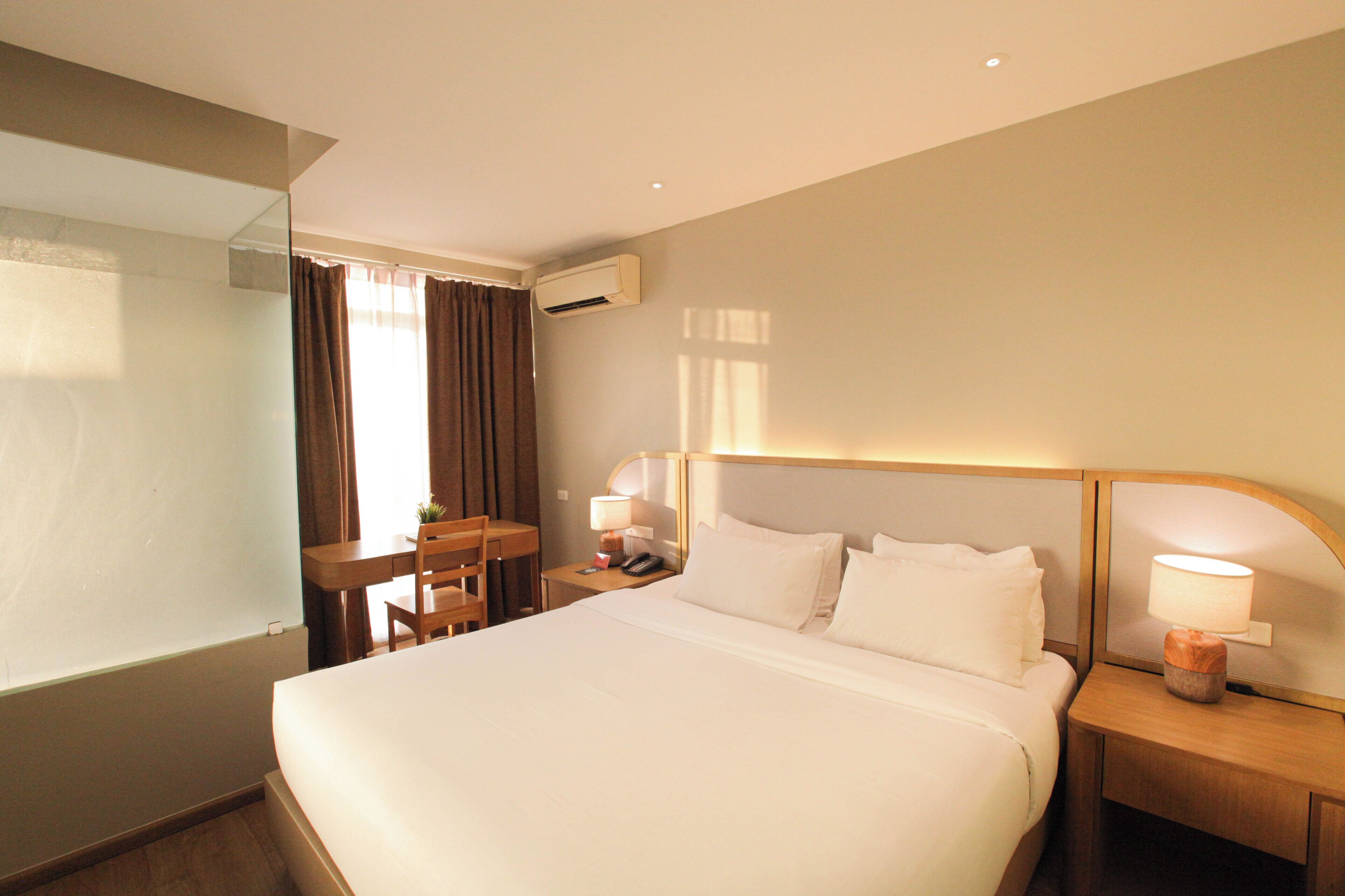 Une chambre d’hôtel avec un grand lit, un bureau avec une chaise, une petite table et une table de chevet avec une lampe.