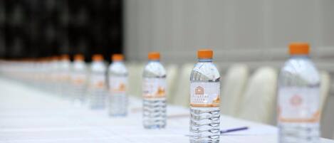 Varias botellas de agua con tapas naranjas sobre una mesa en un salón de conferencias.