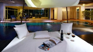 A poolside lounge with a white sofa, pillows, a bottle, glasses, and magazines. - Brighton Hotel Bangkok (Bangkok)