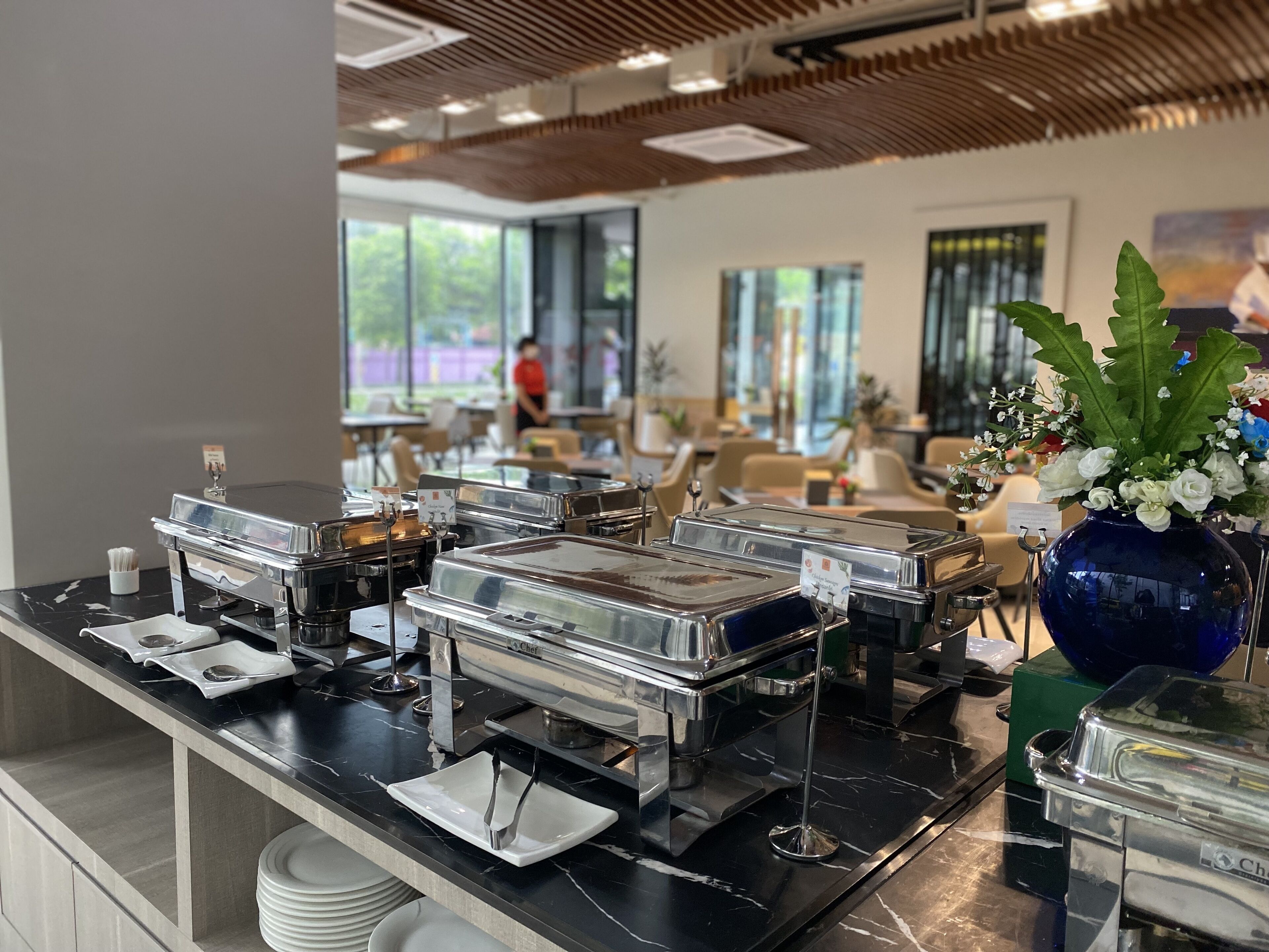 A buffet setup with multiple serving stations, a decorative vase with flowers, and a view of the outdoor seating area.