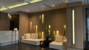 A modern lobby with a reception desk, two sofas, a potted plant, and a wooden wall with vertical lighting. - Brighton Hotel Bangkok (Bangkok)