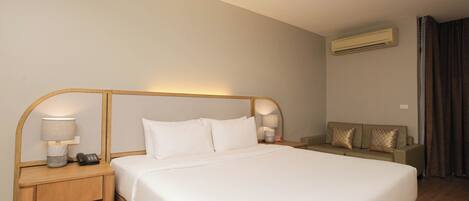 A hotel room with a large bed, two bedside tables with lamps, a sofa, and an air conditioning unit.