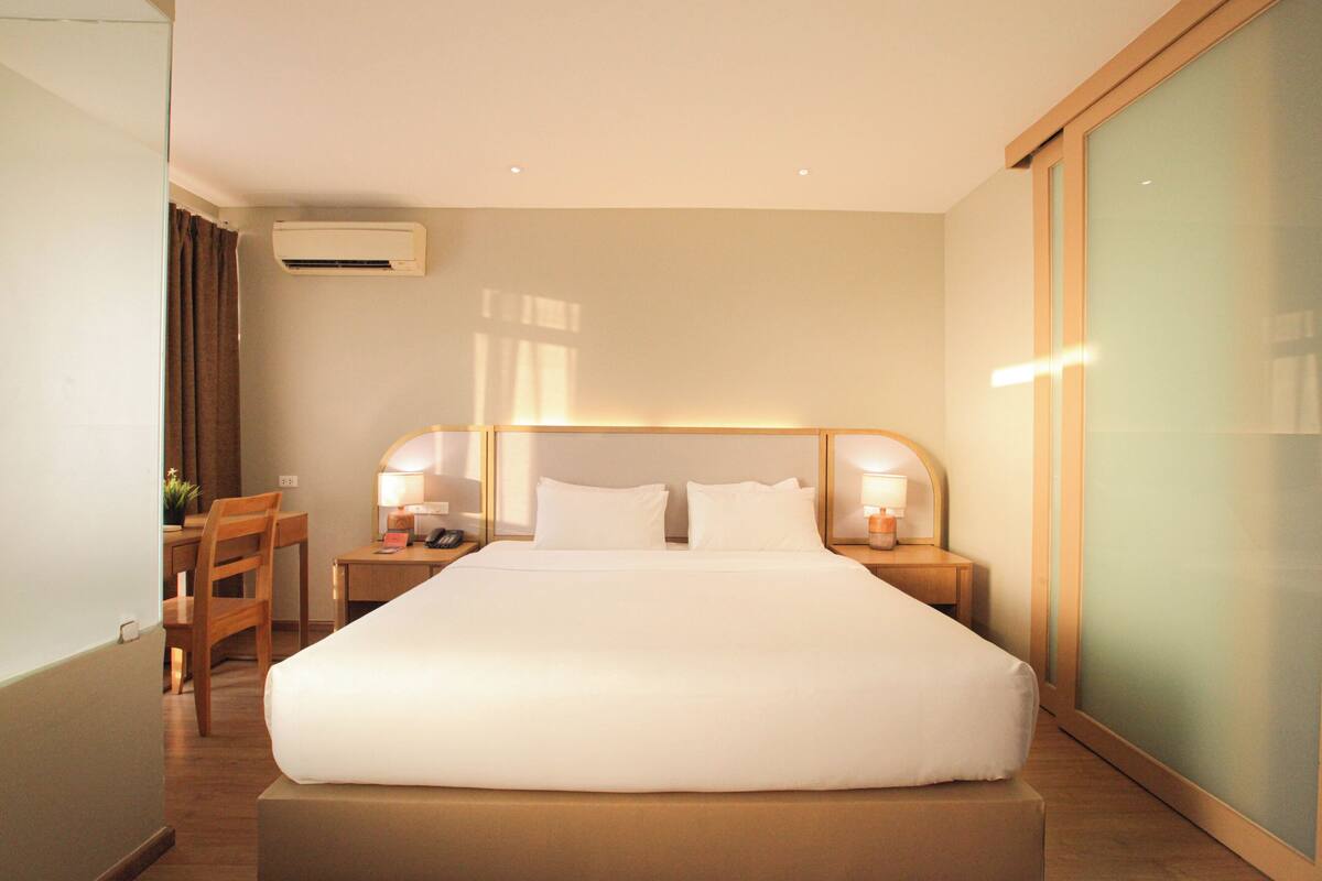 Une chambre d’hôtel avec un grand lit, des tables de chevet avec des lampes, un bureau et une chaise.