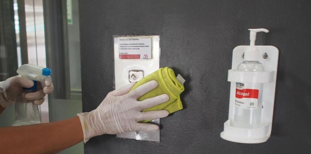 A person cleaning a wall with a spray bottle and a yellow cloth, and a dispenser with a pump.