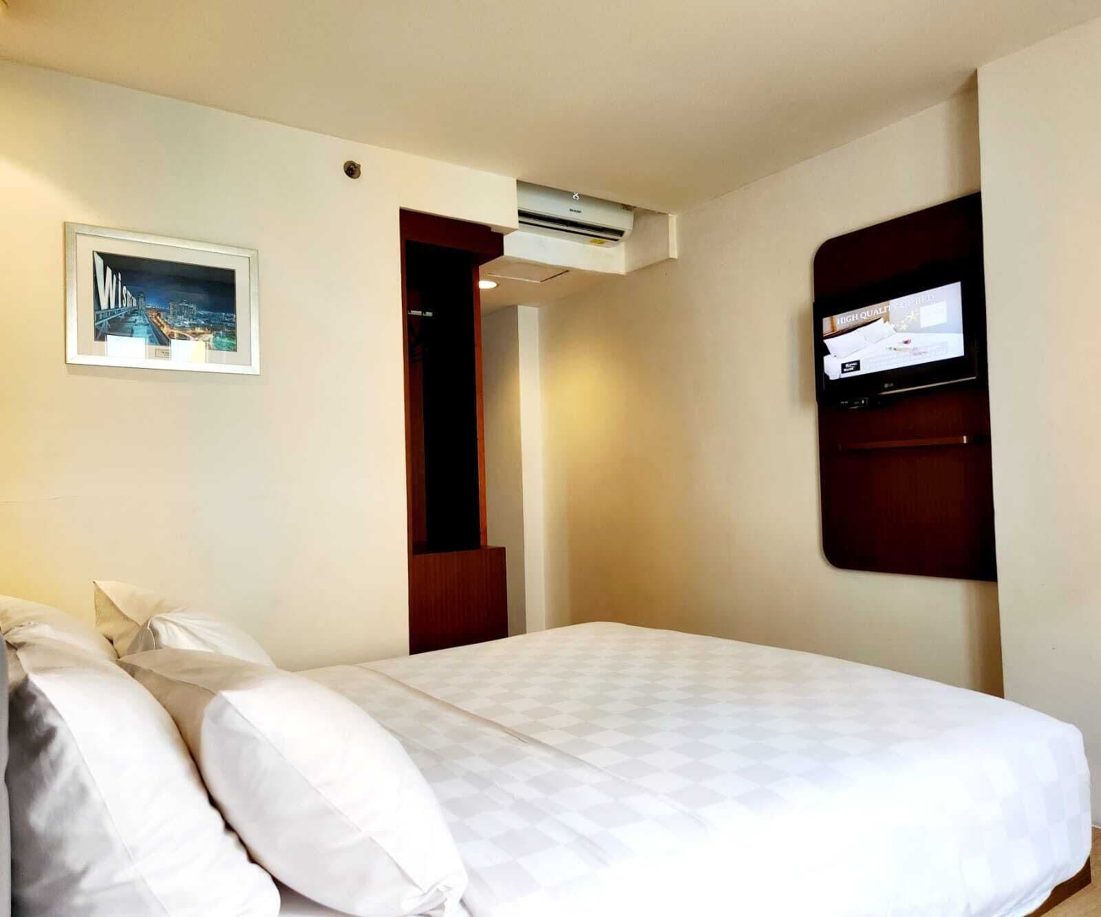 Habitación de hotel con una cama, un televisor montado en la pared y un cuadro enmarcado.