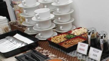 A buffet setup with multiple white bowls and plates, a tray of utensils, and labeled containers of Kecap Manis and Kecap Asin.