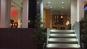 Entrada de hotel con una escalera que conduce al vestíbulo, plantas en macetas y una alfombra roja.
