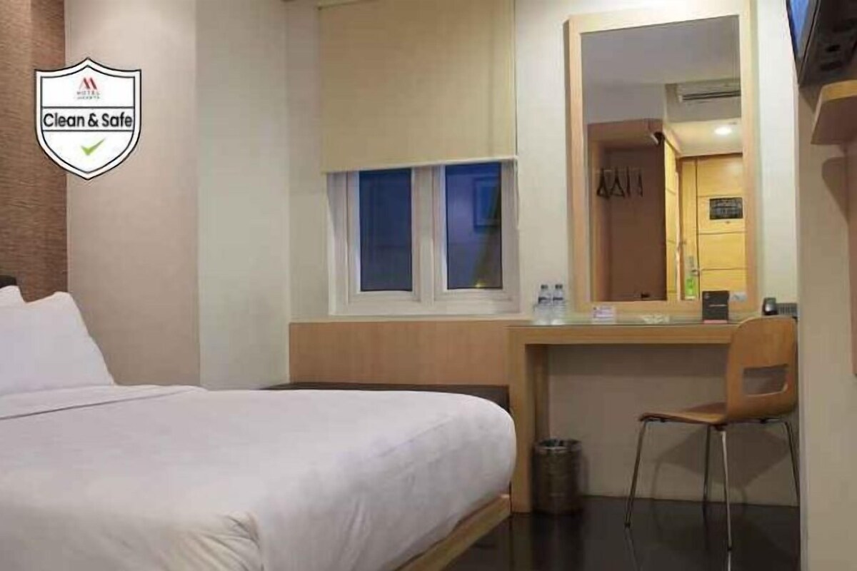 A hotel room with a bed, a desk, a chair, a window, and a mirror.