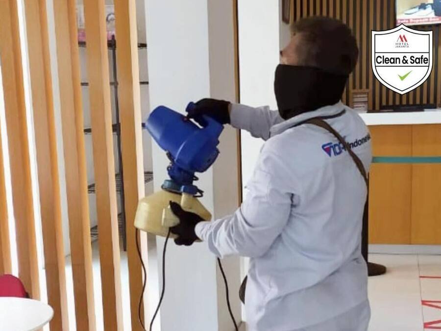 A person in a white uniform spraying a cleaning solution on a wooden partition.