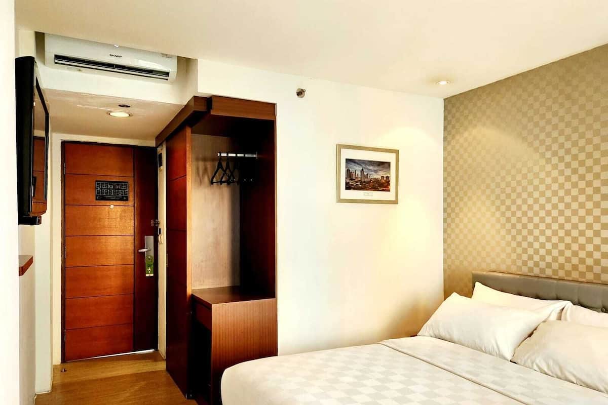 A hotel room with a bed, a wardrobe, a coat rack, and a framed picture on the wall.