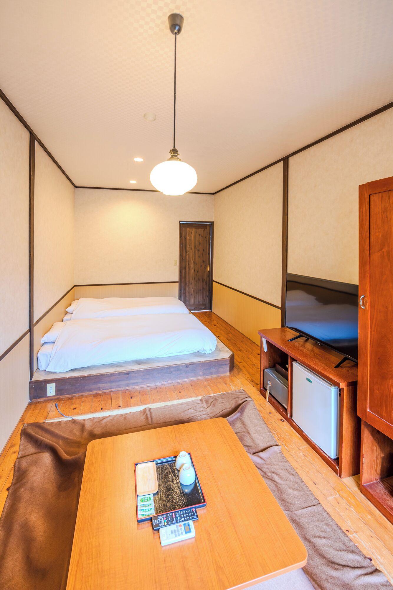 A compact room with a bed, a television, a small cabinet, and a table with a remote control.