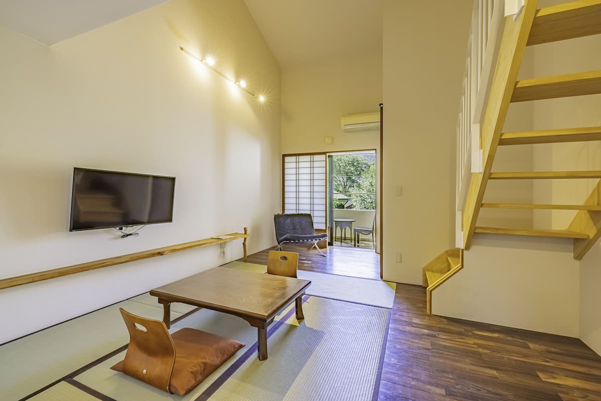 A spacious room with a wooden table, a sofa, a TV mounted on the wall, and a staircase.