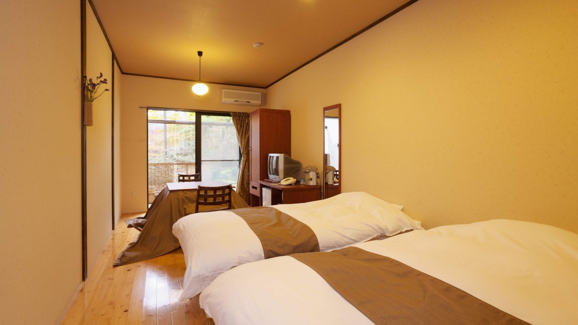 Habitación de hotel con dos camas, un escritorio con teléfono, televisión y ventana con vista a zonas verdes.