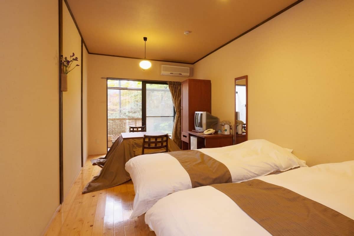 A hotel room with two beds, a desk with a telephone, a television, and a window with a view of greenery.