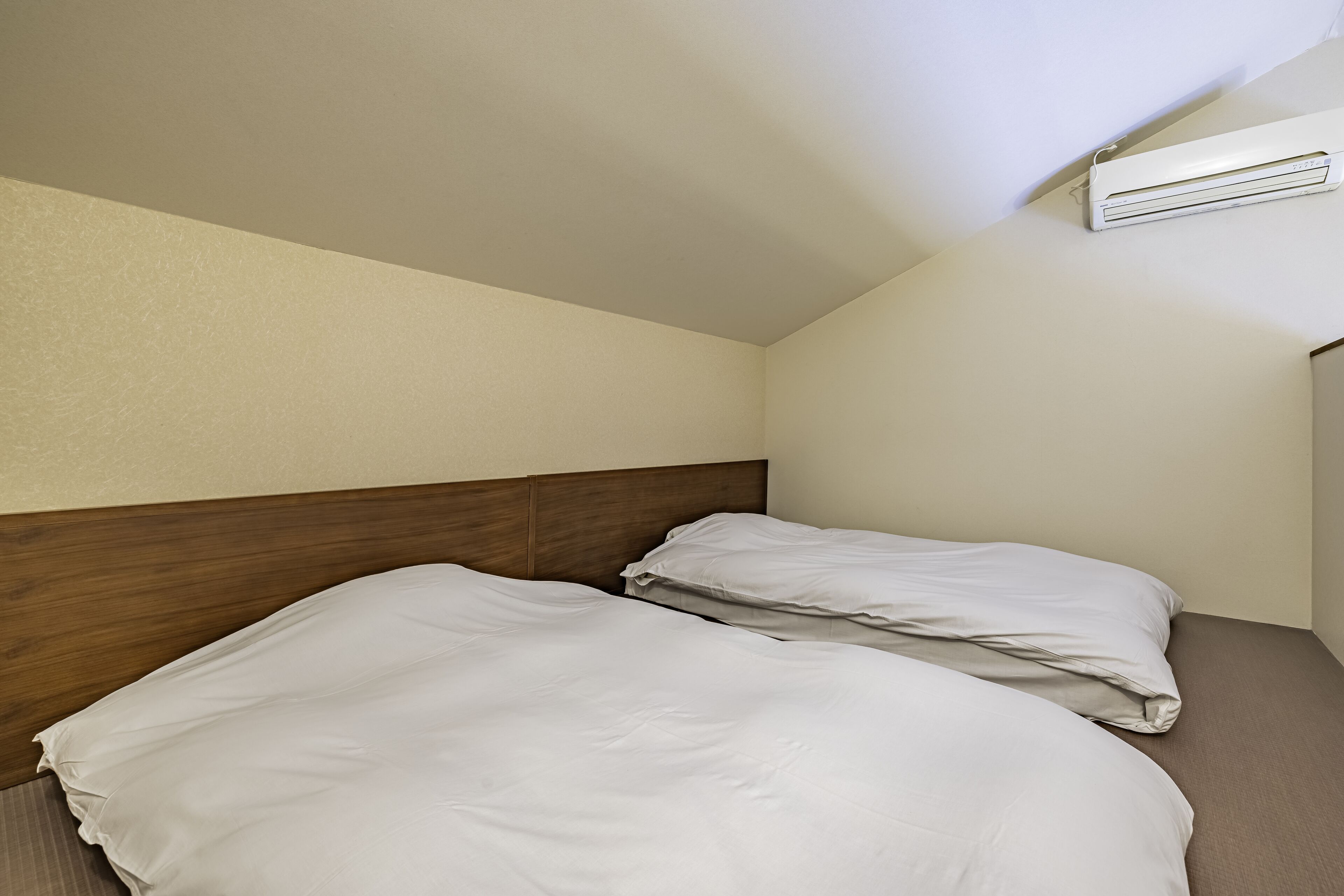 A hotel room with two beds, a wooden headboard, and an air conditioning unit on the wall.