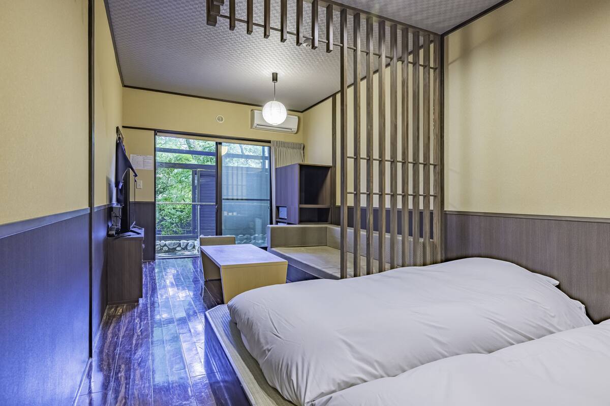 A hotel room with a bed, a desk, a chair, a TV, and a sliding door to a balcony.