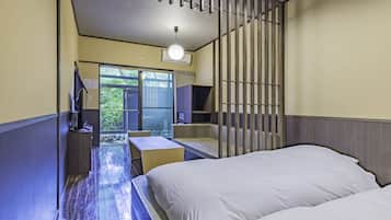 Habitación de hotel con cama, escritorio, silla, televisor y puerta corrediza a un balcón.