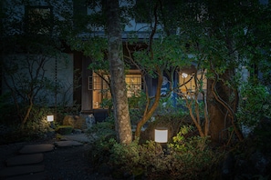 A traditional Japanese-style building with a stone pathway leading to the entrance, surrounded by lush greenery and illuminated by soft lighting. - Shinanoki Ichinoyu (Hakone)