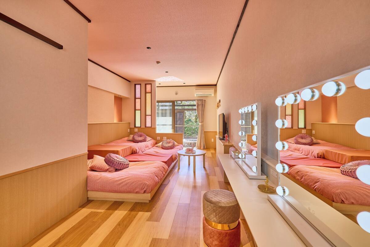 A hotel room with two beds, a vanity with mirrors, a small table, and a view of the outdoors.