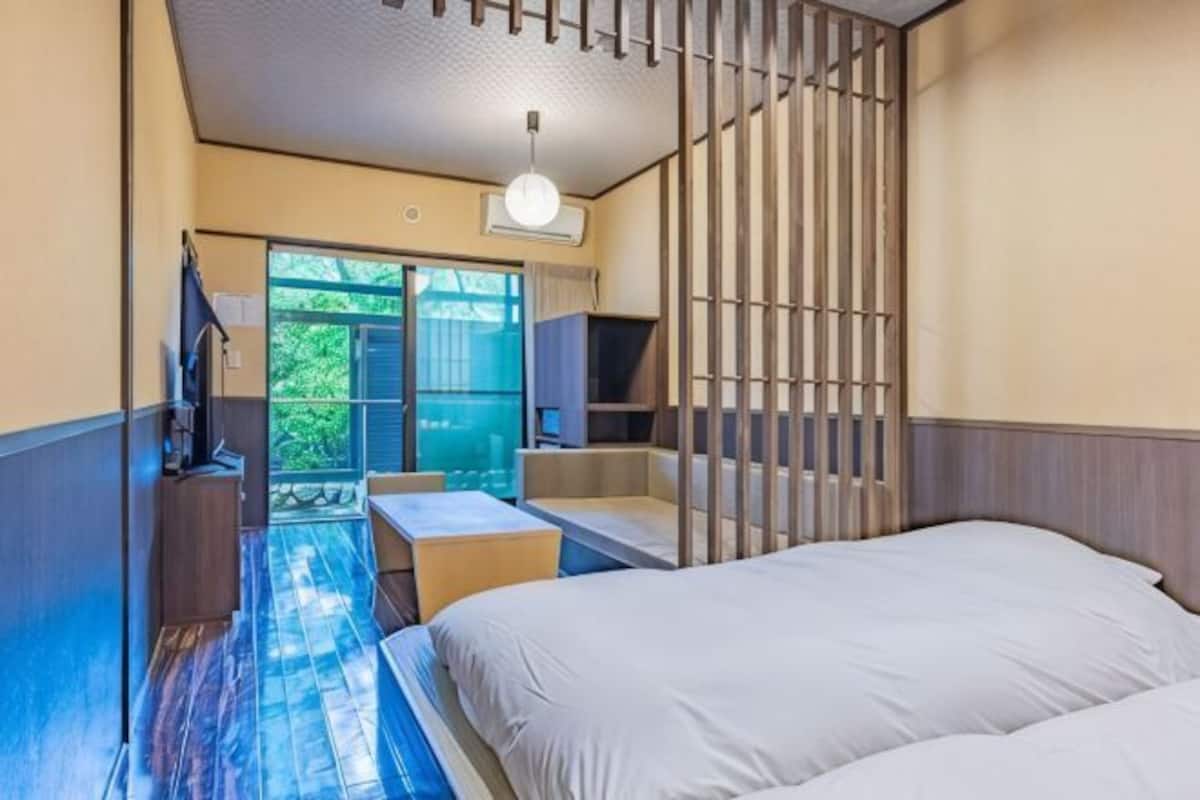 A bedroom with a bed, a desk, a chair, a TV, and a sliding door leading to a balcony.