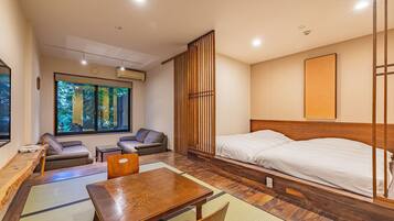 A modern hotel room with a large bed, a wooden table, a sofa, and a view of trees through the window.