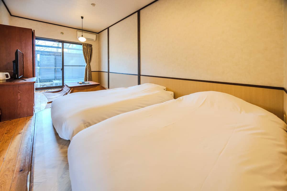 A hotel room with two beds, a wooden desk, a window with curtains, and a ceiling light.