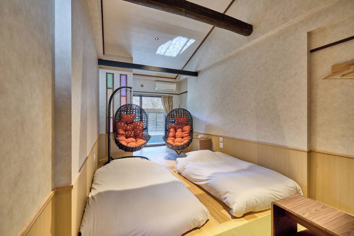 A room with two beds, a small wooden table, and two hanging chairs.