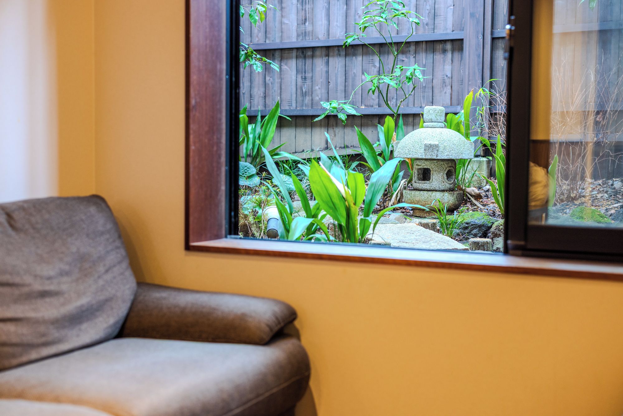 A room with a window overlooking a garden area, a brown chair, and a small stone structure.